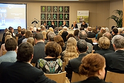 Publikum im Konferenzraum schaut auf Vortragenden und Präsentation