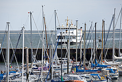 Ein Segelyachthafen im Vordergrund. Eine Fähre und das Meer im Hintergrund.